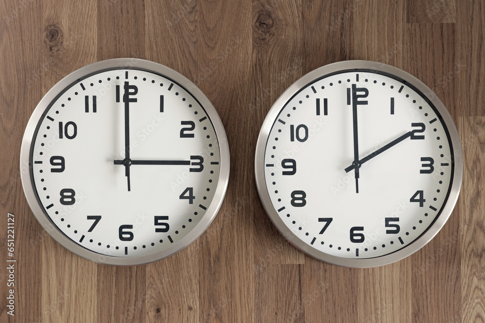 Two clocks, one showing three o'clock, the other showing two o'clock. Time change symbol. Moving the hands backward in autumn to normal time. Two clocks, one showing three o'clock, the other showing two o'clock. Time change symbol. Moving the hands backward in autumn to normal time.