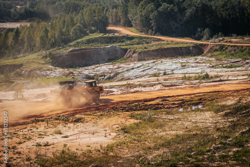 A heavy machine with a trailer works in a sand quarry. The excavator loads sand and clay into the machine.