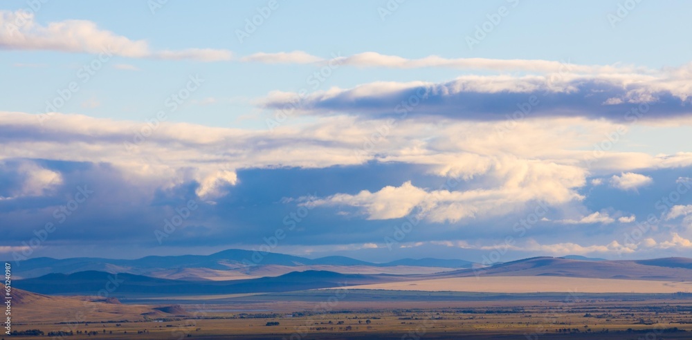 Panoramic landscape with Khakassia steppe under sky with heavy clouds at early autumn day in Siberia, Russia. Cloud shadows lie on the ground