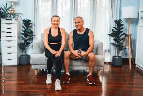 Athletic and sporty senior couple portrait in sportswear sitting on sofa as home exercise concept. Healthy fit body lifestyle after retirement. Clout