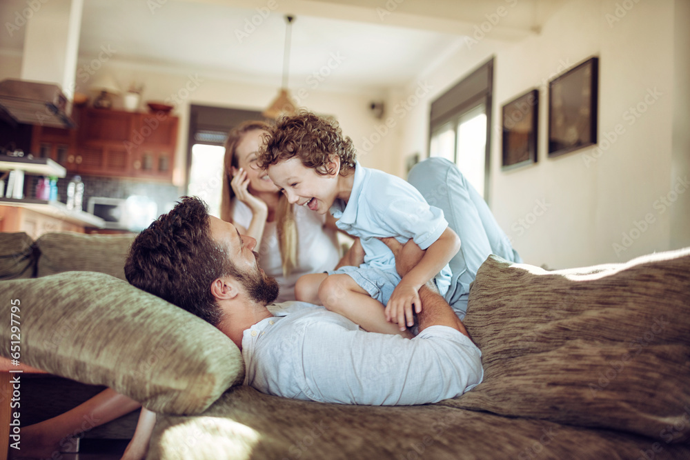 Happy young family being playful and having fun on the couch in the living room at home