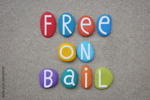 Free on Bail, creative text composed with multi colored stone letters over beach sand