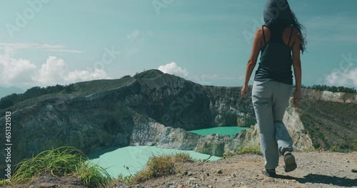 Woman tourist walking to Kelimutu blue crater lakes mountain edge. Back view of long hair girl in trekking clothes with hair blowing on wind. Travel, tourism, holiday, hiking, relax. Slow motion 4K photo