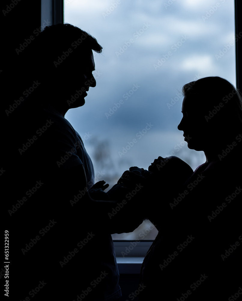 Shadows of young family with newborn. Silhouettes of happy parents.