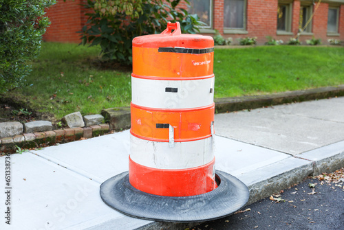 orange construction cone on urban street, symbolizing road safety, caution, and ongoing infrastructure work, with blurred cityscape in background