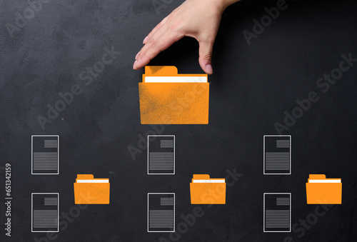 A hand holds a yellow folder over a black background with several folders and documents scattered around. Concept of control and systematization of documents photo