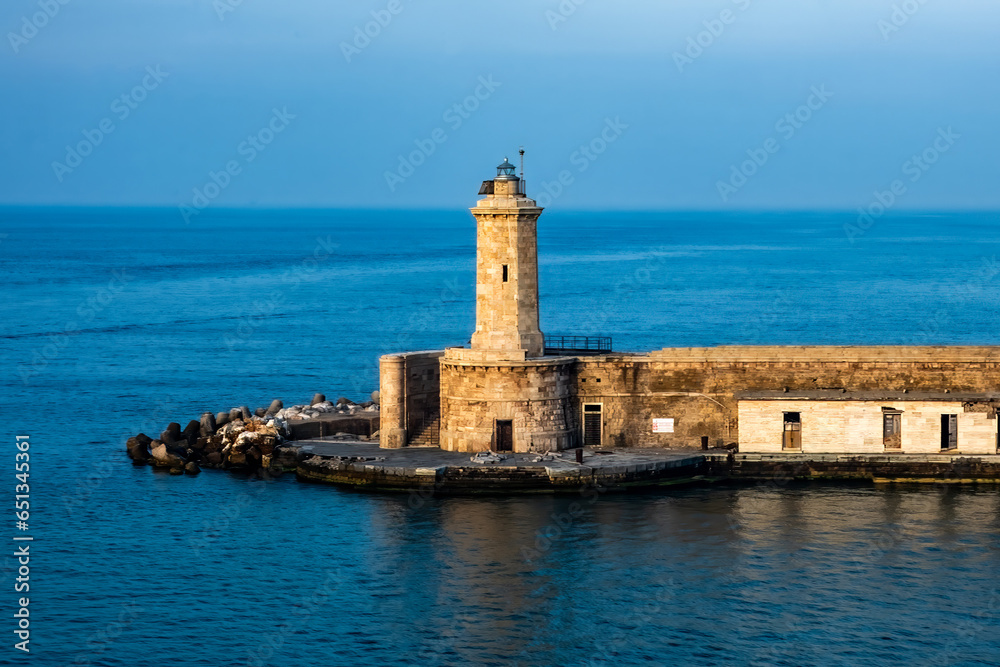 One of the Livorno, Italy lighthouses in the golden glow of the morning sun. Still water and blue sky contrast with the warm sunlight.