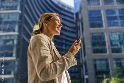 Stylish woman freelancer using phone whiile standing on modern building background  photo