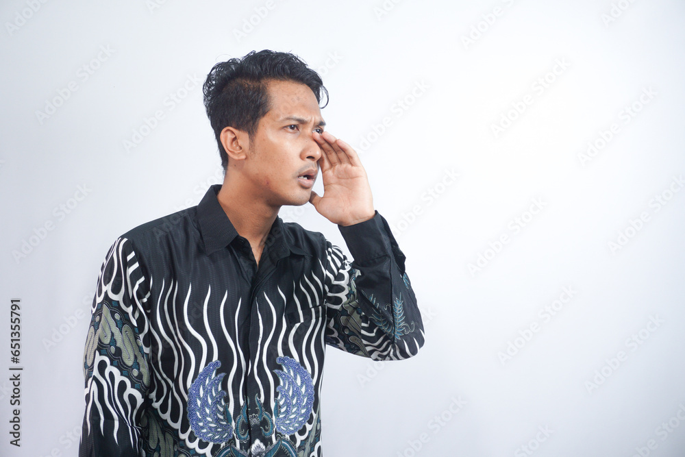 Young asian man wearing batik whispering and gossiping, side view isolated on white Young asian man wearing batik whispering and gossiping, side view isolated on white