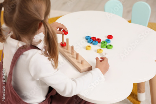 Little girl playing with stacking and counting game at white table indoors. Child's toy