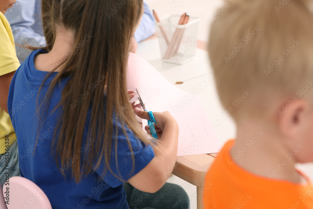 Little girl and boy cutting color paper with scissors at desk, closeup. Kindergarten activities Little girl and boy cutting color paper with scissors at desk, closeup. Kindergarten activities