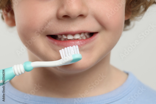 Cute little boy brushing his teeth with plastic toothbrush on white background, closeup