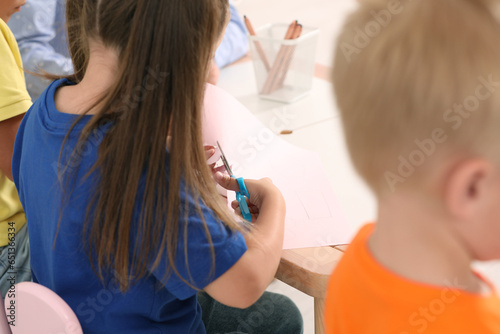 Little girl and boy cutting color paper with scissors at desk, closeup. Kindergarten activities