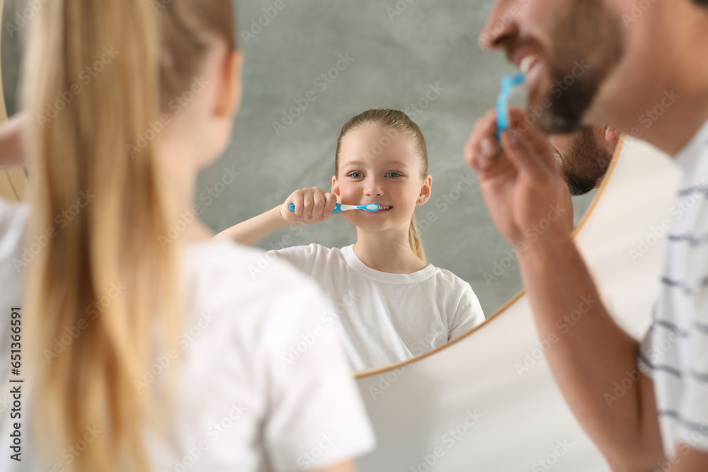 Father and his daughter brushing teeth together near mirror indoors Father and his daughter brushing teeth together near mirror indoors