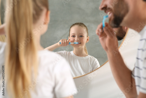 Father and his daughter brushing teeth together near mirror indoors