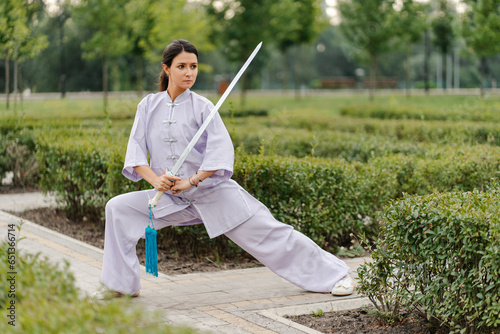 Martial arts woman practicing wushu kung-fu with sword at green park photo