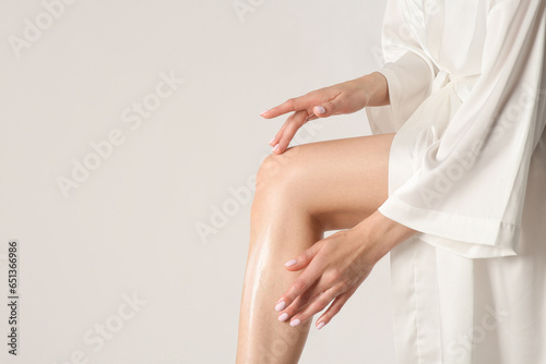 Foto Woman applying body cream onto her smooth legs on white background, closeup