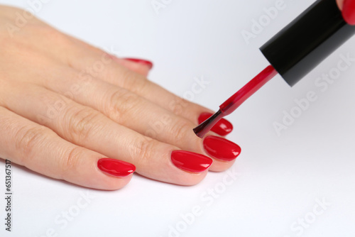 Woman painting nails with red polish on white background  closeup