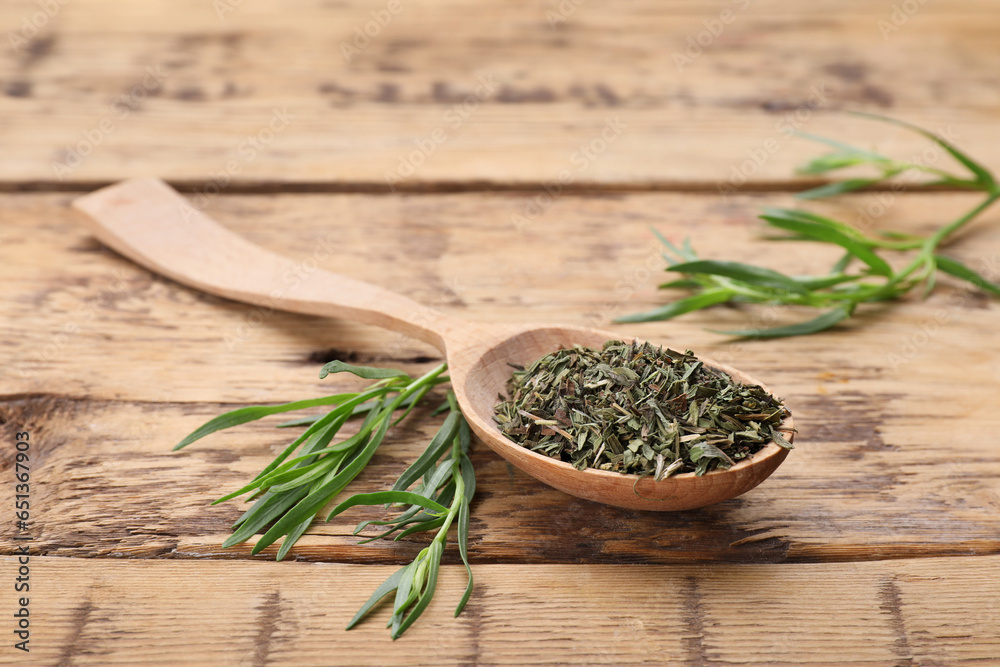 Spoon of dry tarragon and green leaves on wooden table Spoon of dry tarragon and green leaves on wooden table