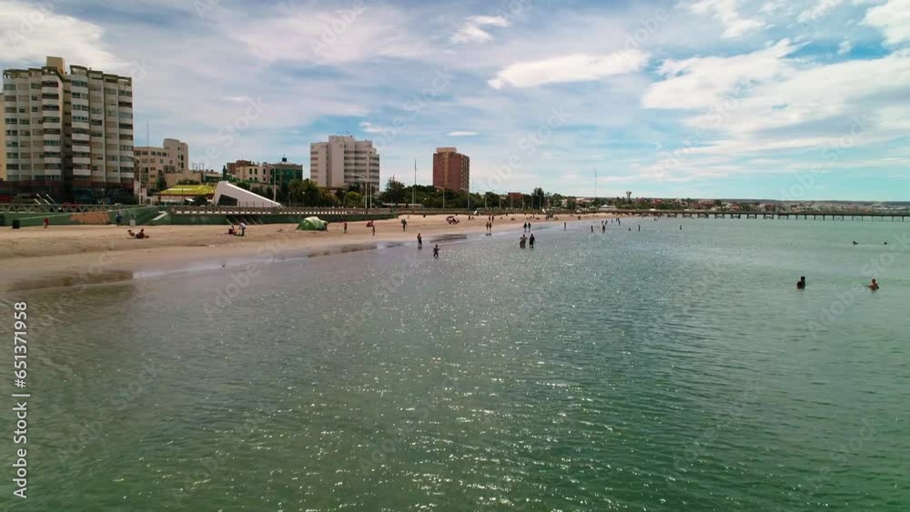 Aerial: Drone Flying Forward Over People Enjoying At Beach Near Buildings In City Against Cloudy Sky - Puerto Madryn, Argentina Aerial: Drone Flying Forward Over People Enjoying At Beach Near Buildings In City Against Cloudy Sky - Puerto Madryn, Argentina