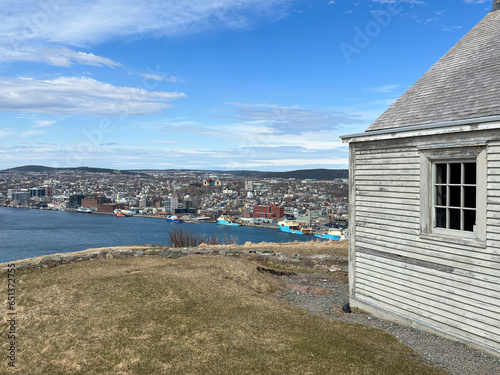 The hillside of St. John's Harbour, on a sunny day, under blue sky and white clouds. The colorful wooden houses are scattered along the hillside with the blue ocean in the foreground.  photo