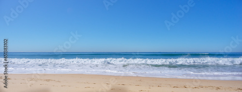 Blue sky, breaking surf waves and sandy beach on a calm sunny day on the water's edge as the tide comes in along the shoreline of Kawana Beach, Sunshine Coast, Queensland, Australia