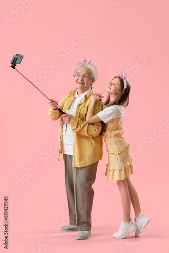 Φωτογραφία Little girl with her grandmother in crowns taking selfie on pink background