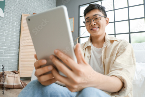 Young Asian man with tablet computer video chatting in bedroom