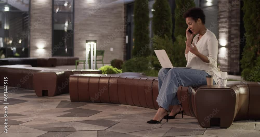 Ethnic businesswoman talking via smartphone and working on laptop outdoors Ethnic businesswoman talking via smartphone and working on laptop outdoors