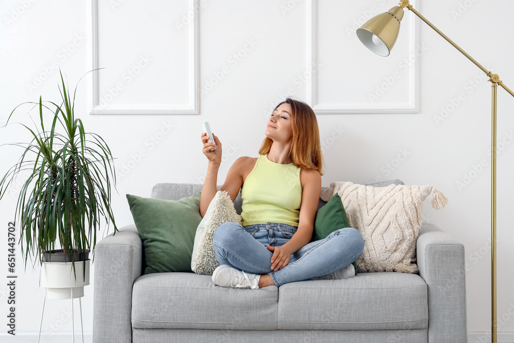 Young woman switching on air conditioner at home Young woman switching on air conditioner at home