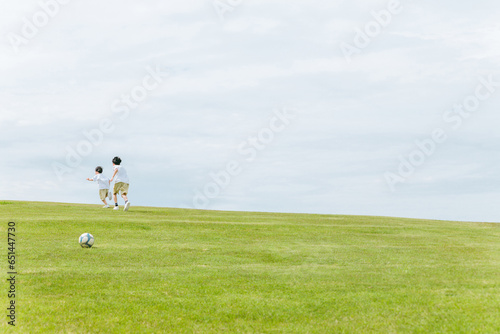 青空の見える公園を走る兄弟の後ろ姿・少年とサッカーボール 