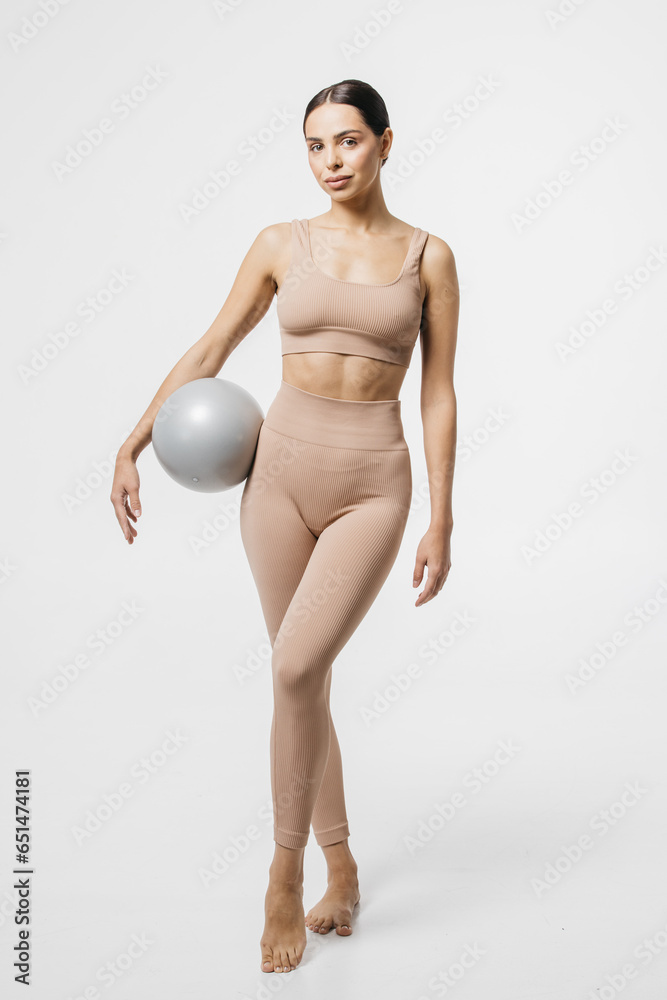 Obraz premium Confident fitness woman posing with medicine ball. Portrait of an attractive sportswoman holding a medical fitness ball and using it on a light studio background.