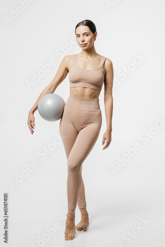 Confident fitness woman posing with medicine ball. Portrait of an attractive sportswoman holding a medical fitness ball and using it on a light studio background.