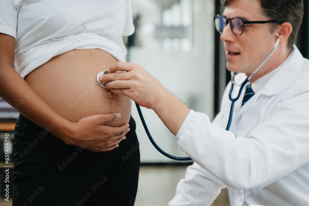 Pregnant african woman has appointment with doctor at clinic. Male gynaecologist OB GYN medic specialist with stethoscope listens to baby's heartbeat in mother's belly. Pregnant african woman has appointment with doctor at clinic. Male gynaecologist OB GYN medic specialist with stethoscope listens to baby's heartbeat in mother's belly.