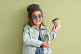 Cute little girl in sunglasses with cup on green background