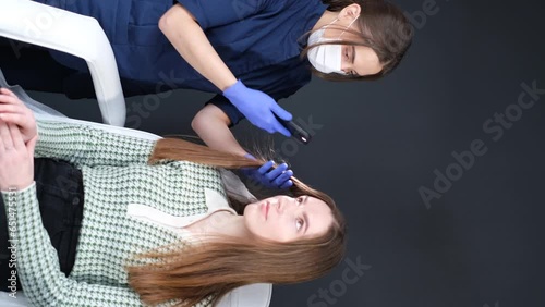 Doctor trichologist examines woman patient's hairs using trichoscope in clinic. Vertical video. photo
