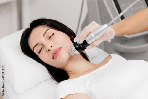 Attractive young woman undergoing a cosmetic procedure in a beauty salon. A woman undergoes fractional RF lifting against a light background. Advertising concept for clean and young facial skin. photo