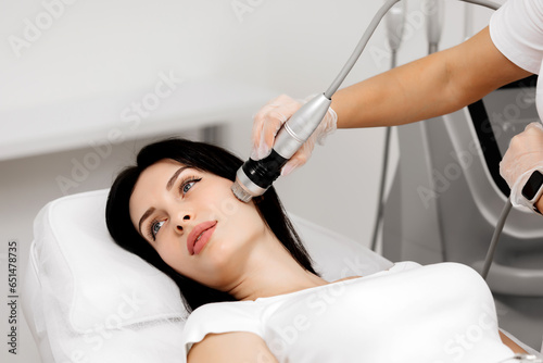 A young woman undergoes a radiofrequency facelift procedure. Facial skin care, anti-aging facial rejuvenation. Radio wave face lifting in a cosmetology clinic.