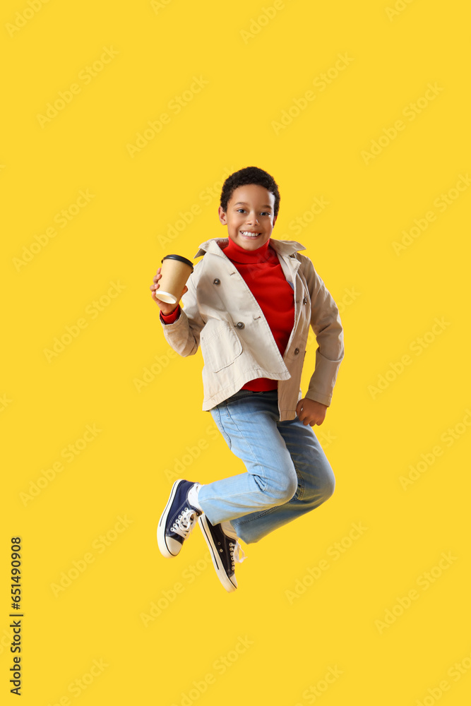 African-American little boy with cup of cocoa jumping on yellow background African-American little boy with cup of cocoa jumping on yellow background