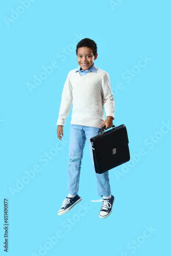 African-American little boy with briefcase jumping on blue background