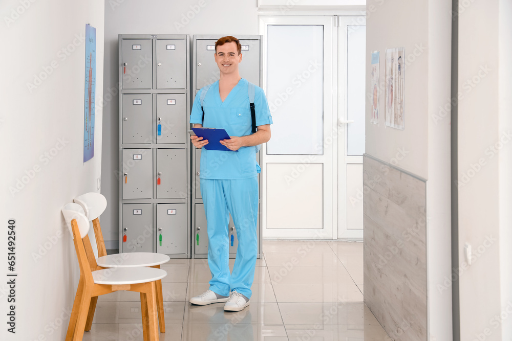 Male medical student with clipboard near locker at university Male medical student with clipboard near locker at university