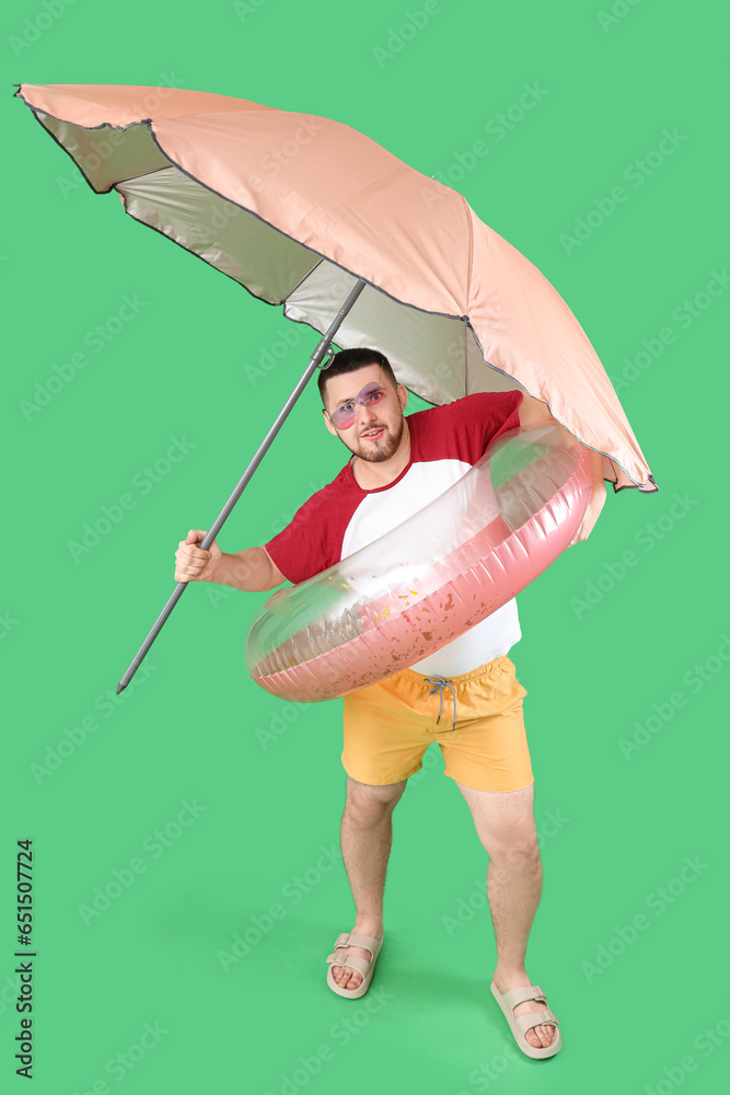 Handsome young man with inflatable ring and umbrella on green background Handsome young man with inflatable ring and umbrella on green background