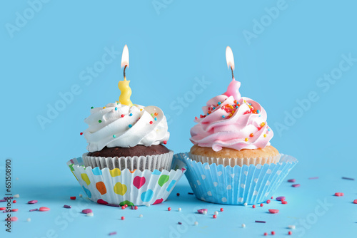 Delicious birthday cupcakes with burning candles on blue background