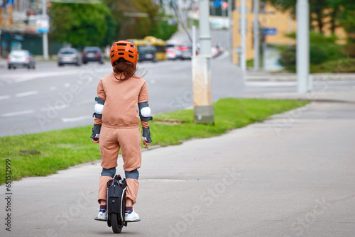 Woman in protective gear riding electric unicycle, monocycle or mono wheel. Trendy woman in helmet on electric vehicle, view from back. Woman ride electric mono wheel, personal electric transport photo