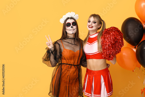 Female friends dressed for Halloween with balloons on yellow background