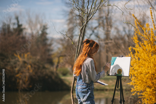 Fototapeta Photo of a woman artist painting outdoors next to a tree