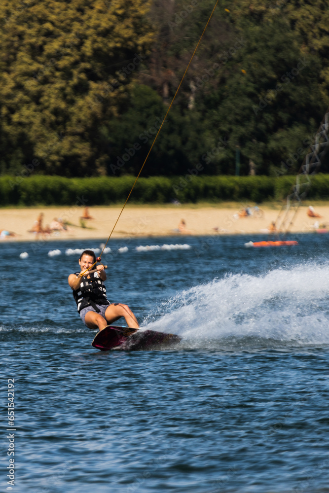 Female wakeboarder wakesurfing. Girl riding waterski cabel. Holding tow rope. Summer activities in the lake.