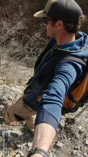selfie vertical video : man hiking down on a trail next to vertical slab. He wears backpack and cap. Video in slow motion