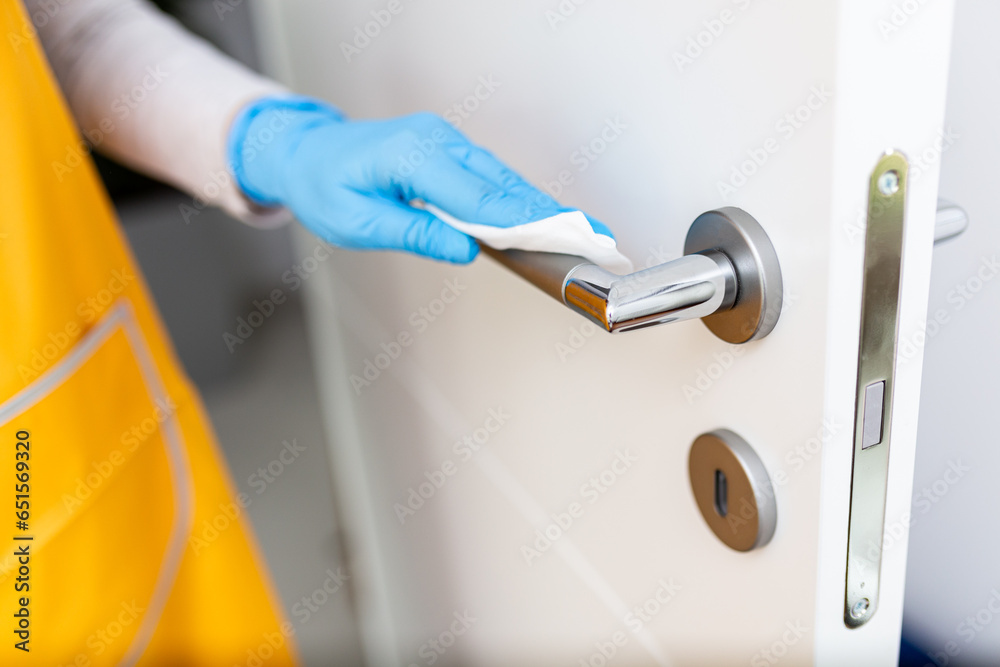 Hand wearing surgical glove while disinfect doorknob with wet wipe - obrazy, fototapety, plakaty 