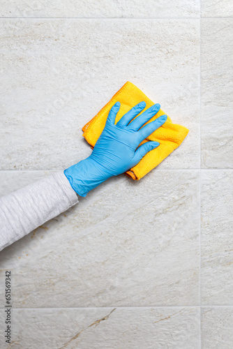 Young woman cleaning ceramic tiles with rag in bathroom.